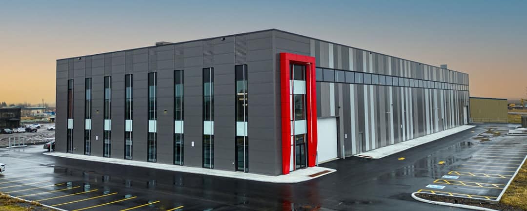 Untitled design (1) Large commercial facility with glass facade and red architectural accent panels